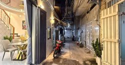 Hẻm nhỏ về đêm với ánh sáng từ ngôi nhà hiện đại bên trái và xe máy dựng trong ngõ