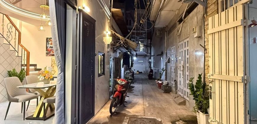 Hẻm nhỏ về đêm với ánh sáng từ ngôi nhà hiện đại bên trái và xe máy dựng trong ngõ