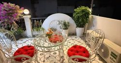 Sân thượng ban đêm với bộ bàn ghế sắt uốn màu trắng, đệm đỏ, cây cảnh và đèn dây trang trí nhà gò vấp dưới 4 tỷ