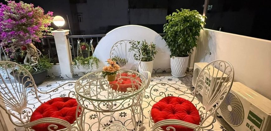 Sân thượng ban đêm với bộ bàn ghế sắt uốn màu trắng, đệm đỏ, cây cảnh và đèn dây trang trí nhà gò vấp dưới 4 tỷ