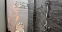 Phòng tắm hiện đại có bồn cầu trắng, vòi sen cây và tường gạch vân đá xám nhà gò vấp