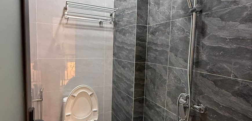 Phòng tắm hiện đại có bồn cầu trắng, vòi sen cây và tường gạch vân đá xám nhà gò vấp